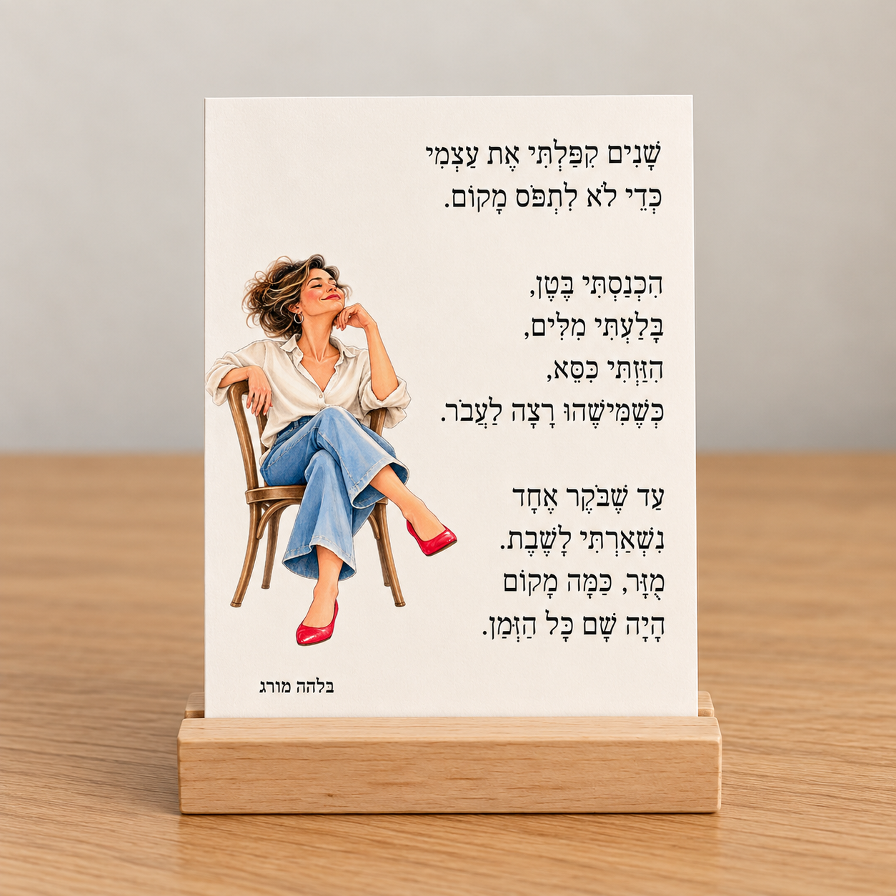 כרטיס השיר שנים קיפלתי את עצמי, מאת בלהה מורג, מונח על מעמד עץ טבעי על שולחן.